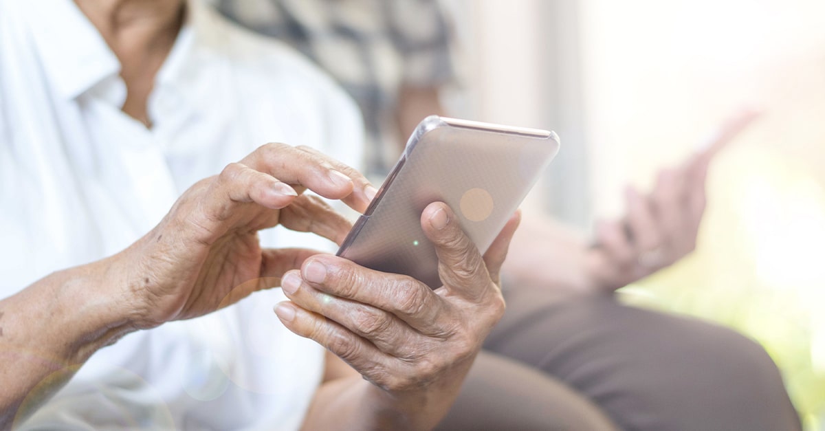 Closeup of elderly woman's hands using a mobile phone with elderly man's hands and phone blurred in the background, illustrating the blog topic of Top Free Apps for Seniors on Medicare
