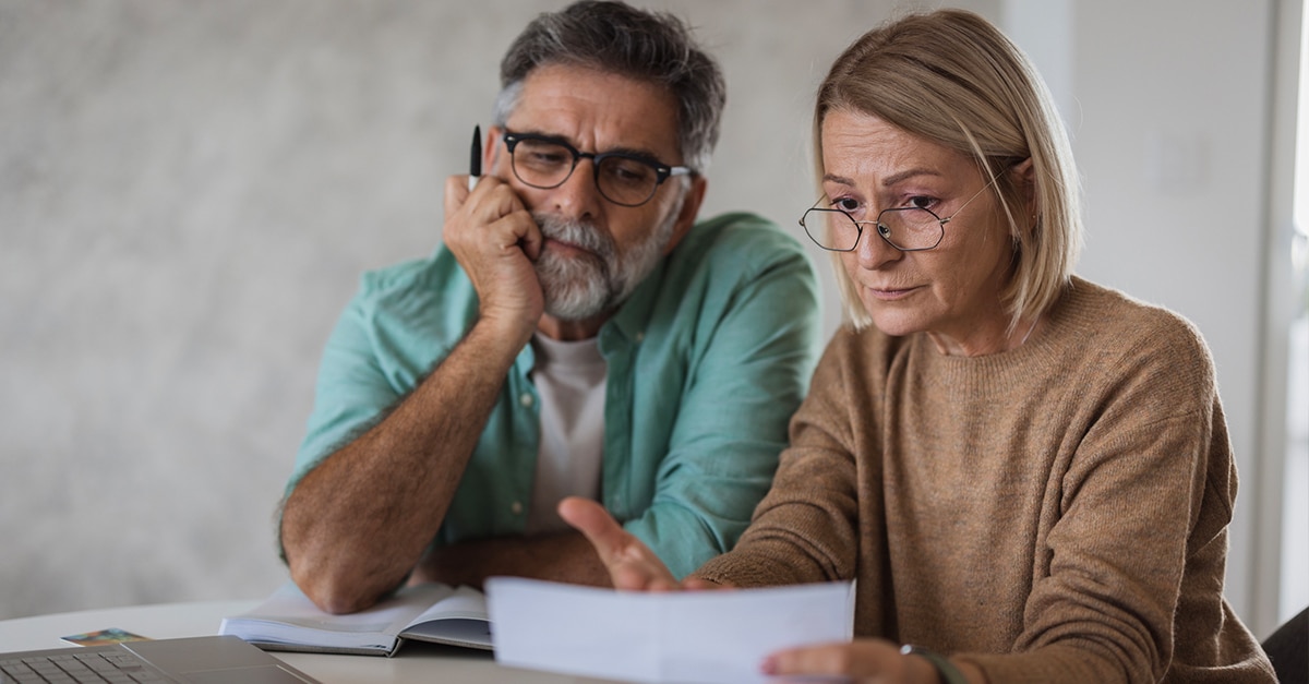 Mature adult couple discussing expenses and bills, looking worried about finances at home