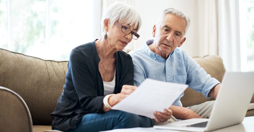 Senior couple reviewing Medicare Advantage paperwork while sitting on a couch at home.