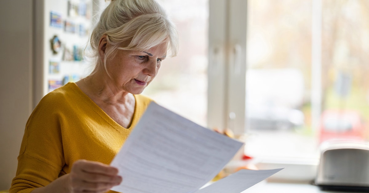 Senior woman standing in kitchen and reviewing her Medicare Summary Notice to check for fraud