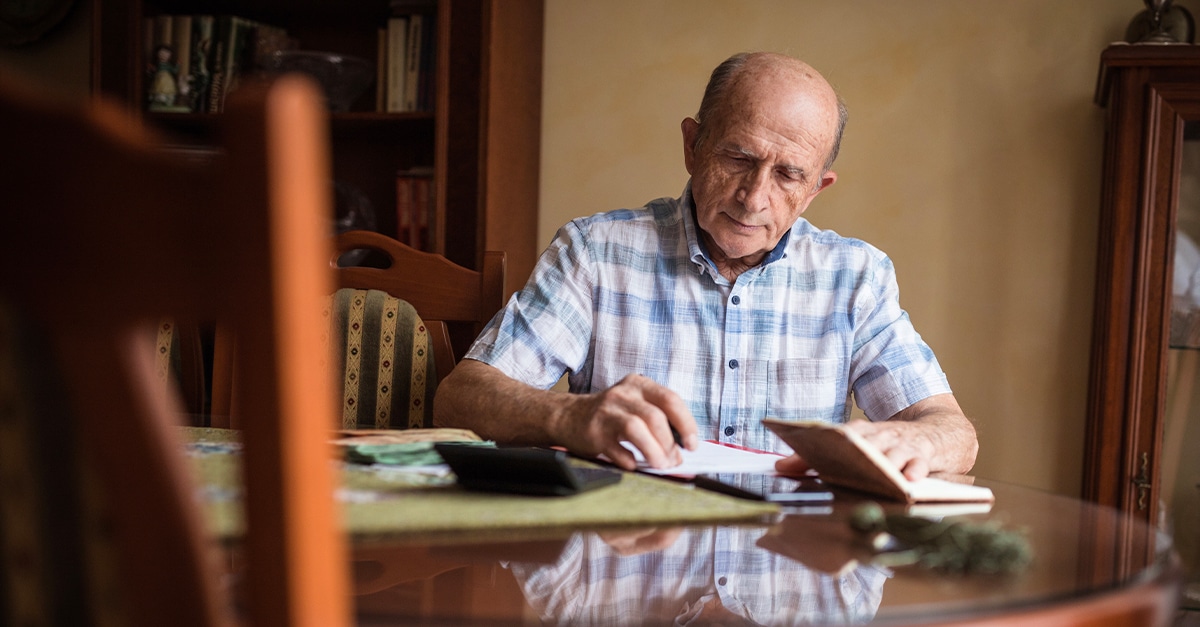Senior man sitting at kitchen table paying bills
